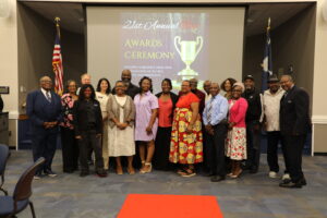 Group photo of people dressed in business professional clothing standing in front of a screen announcing the 21st Annual TRIO Awards and Recognition Ceremony.