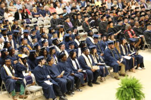 Graduates in navy blue gowns and mortar board hats occupy the first 5 rows of seating.