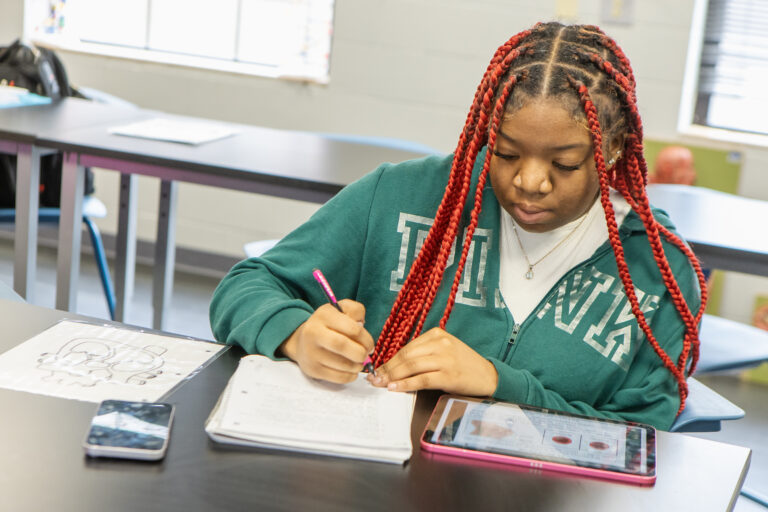 A young girl sitting in class writing in a notebook.