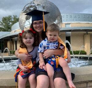 Kyra Van Anda, graudate sitting by fountain with children