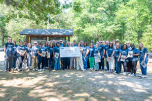 A gourp of diverse people stand in front a state park sign holding a large donation check.
